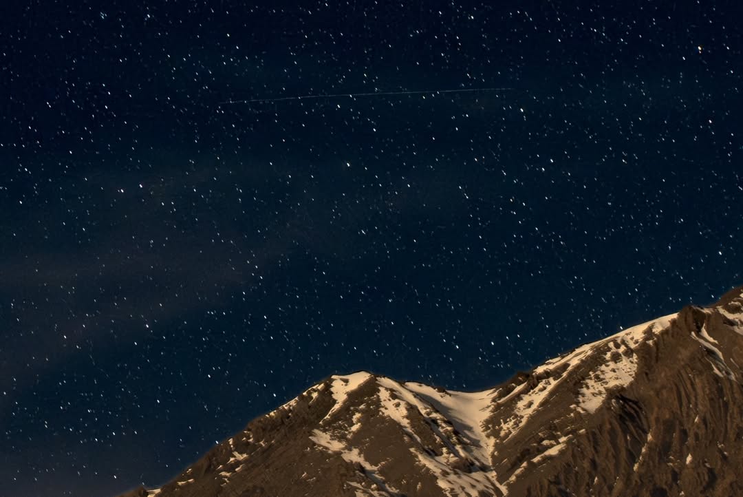 Stars over moonlit, snow-capped mountain peaks at night (2/3)